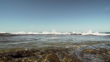pequeñas olas rodando sobre una formación rocosa de lava que crea una barrera de coral y una piscina de marea