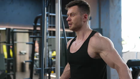muscular athlete training in gym. handsome guy with sportive body exercising hard near the simulator in modern fitness center. slow motion.
