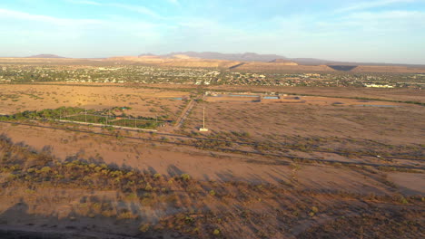 Aerial-over-brown-fields-at-golden-hour,-Green-Valley,-Arizona-in-background