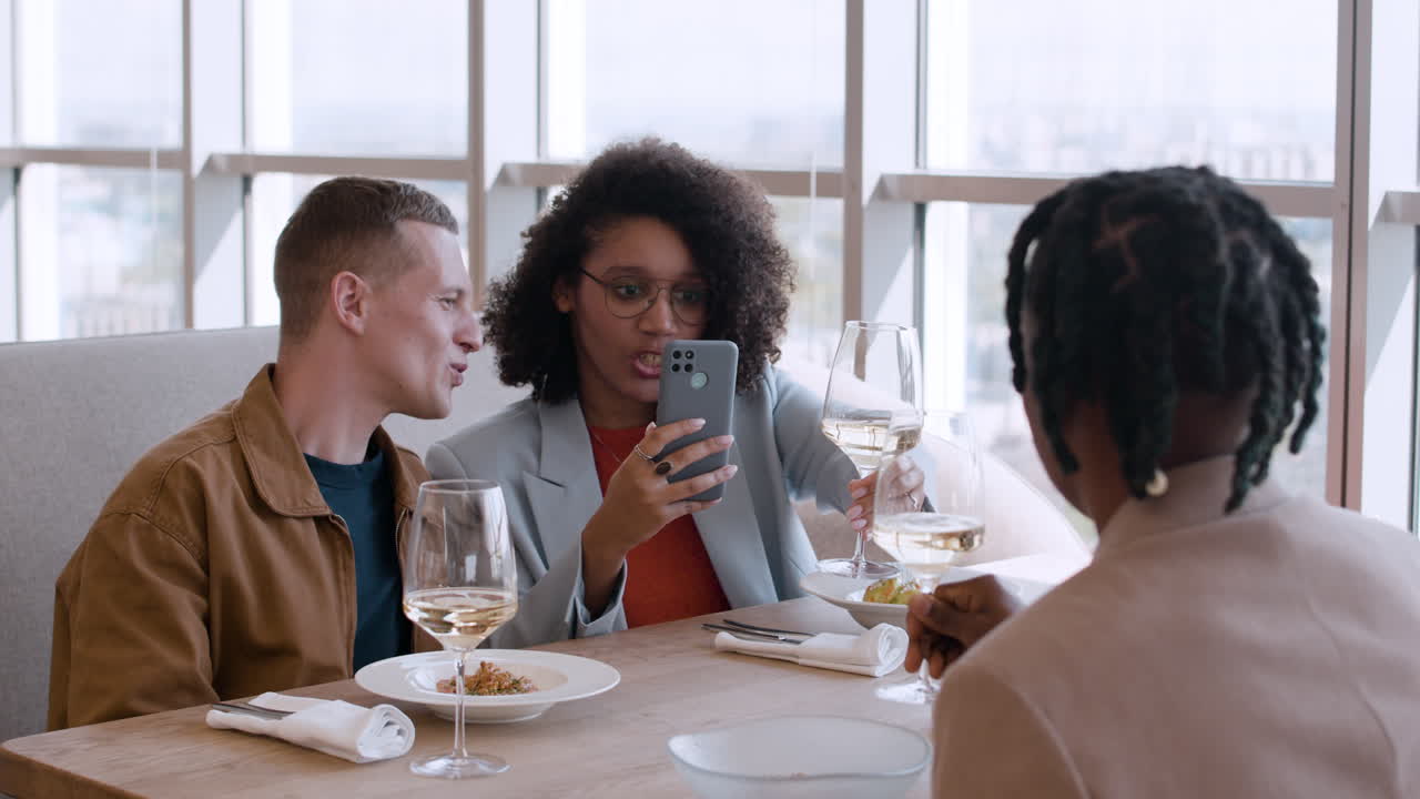 Friends enjoying a meal and looking at a phone in a restaurant.