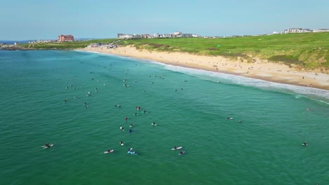 fistral beach surfers sit and wait for ocean waves in newquay, aerial orbital panning shot, cornwall, uk