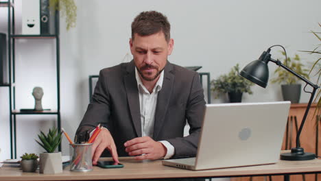 Businessman-working-with-documents-at-office-desk,-taking-a-break,-playing-smartphone-online-games