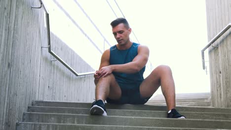 Young-Man-Massaging-Injured-Leg-Sitting-on-Stairs.fitness,-sport-and-health-concept-young-man-massaging-injured-leg-or-knee-sitting-on-stairs