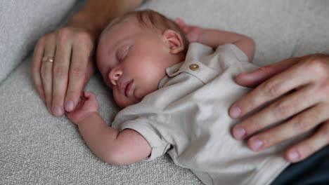 adorable newborn sleeps on the bed holding hands up. male hands stroke child's belly. close up.