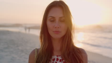 portrait of beautiful young woman enjoying warm summer day on beach sunset background looking at camera