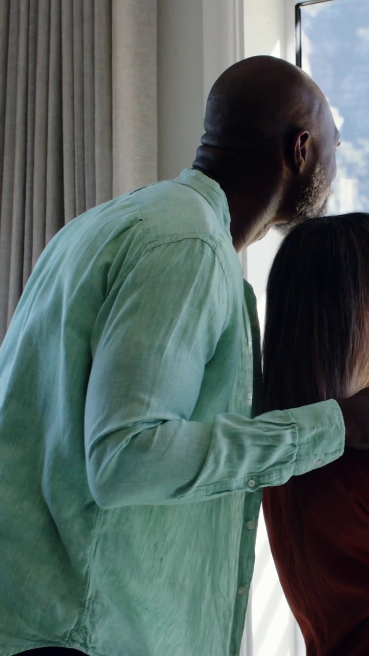 Vertical video: Entering man in green top at home window, watching trees, resting hand on her