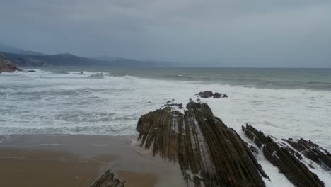 Thin-sharp-layered-rocks-extend-into-ocean,-flysch-itzurun-zumaia-spain,-aerial-reverse-dolly