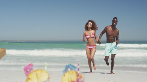 african american couple running side by side at beach