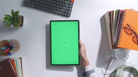 vista de arriba hacia abajo de una computadora portátil con pantalla verde simulada pantalla chromakey en un escritorio de oficina de madera al lado de la libreta con bolígrafos, gafas y un vaso de agua.