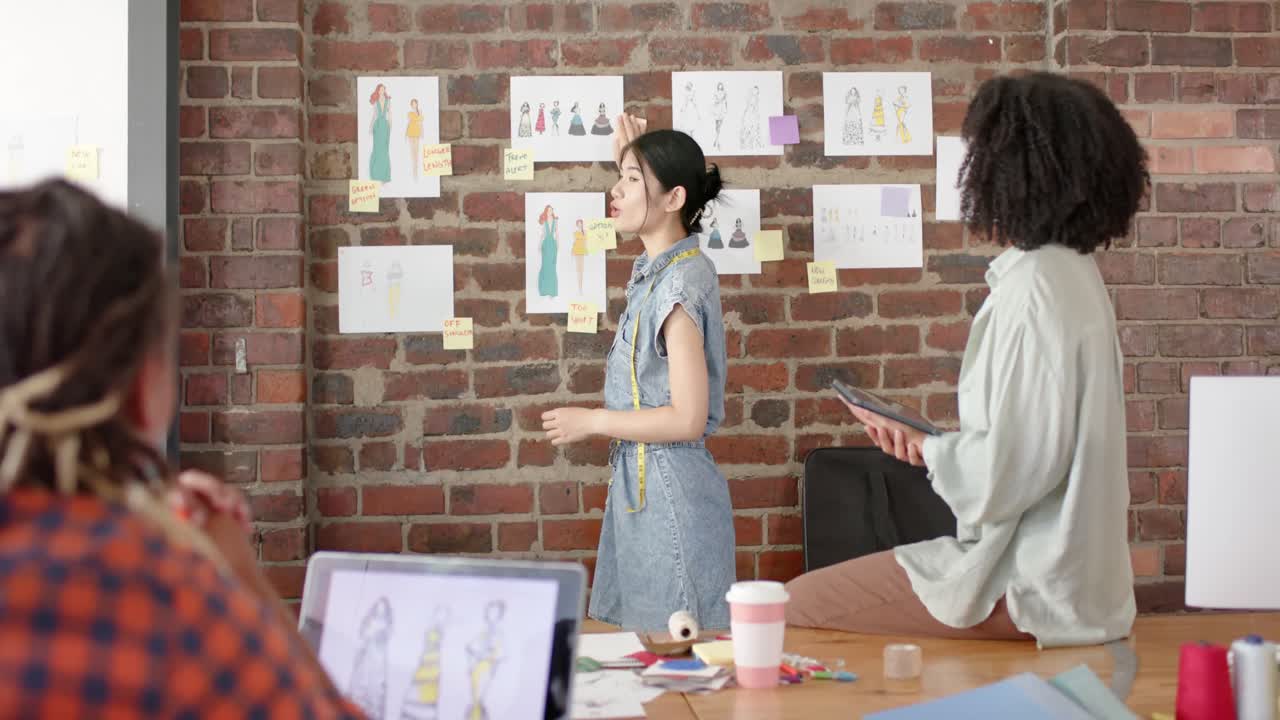 diversos diseñadores ocupados usando tablets y discutiendo el trabajo en el estudio de diseño de moda en cámara lenta