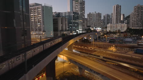 follow shot of train passing overpass and traffic in kwai chung district of hong kong at blue hour