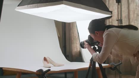 asian female photographer walking into home studio and taking photos of women's shoes