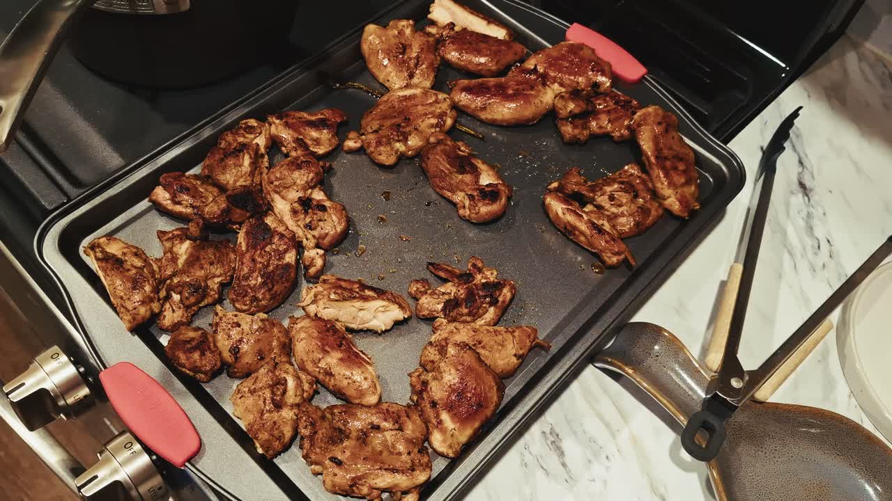 Grilled chicken pieces sizzling on a stovetop griddle pan in a home kitchen setting