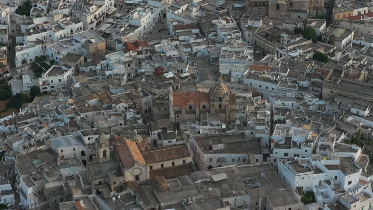 Ripresa aerea dall'alto con rotazione sulla storica città bianca di Ostuni al crepuscolo, che mostra edifici densi, tetti e cupole di chiese, Puglia, Italia