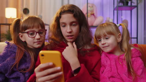 Three-siblings-children-girls-using-smartphone-texting-messages-on-social-media-applications-online