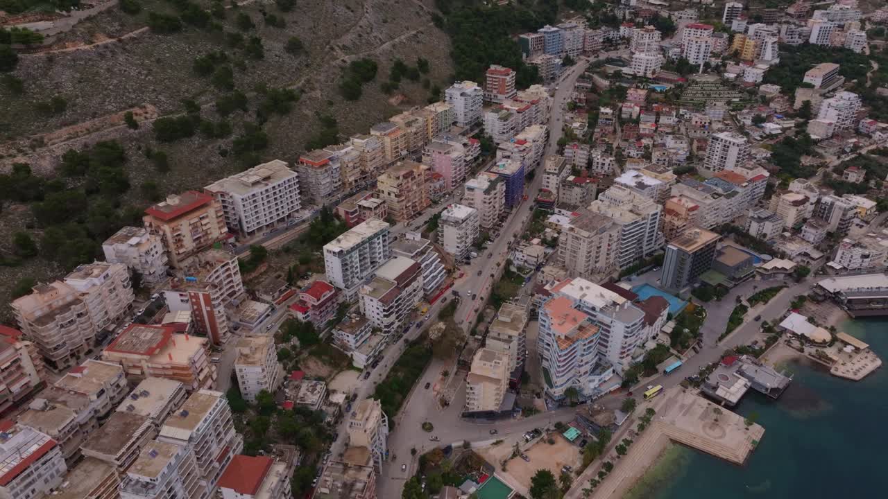 Vista de drone de uma cidade costeira com paisagens mediterrâneas e colinas, Albânia