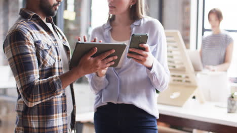 African-American-man-and-Caucasian-woman-discuss-business-over-a-tablet-and-smartphone-in-an-office