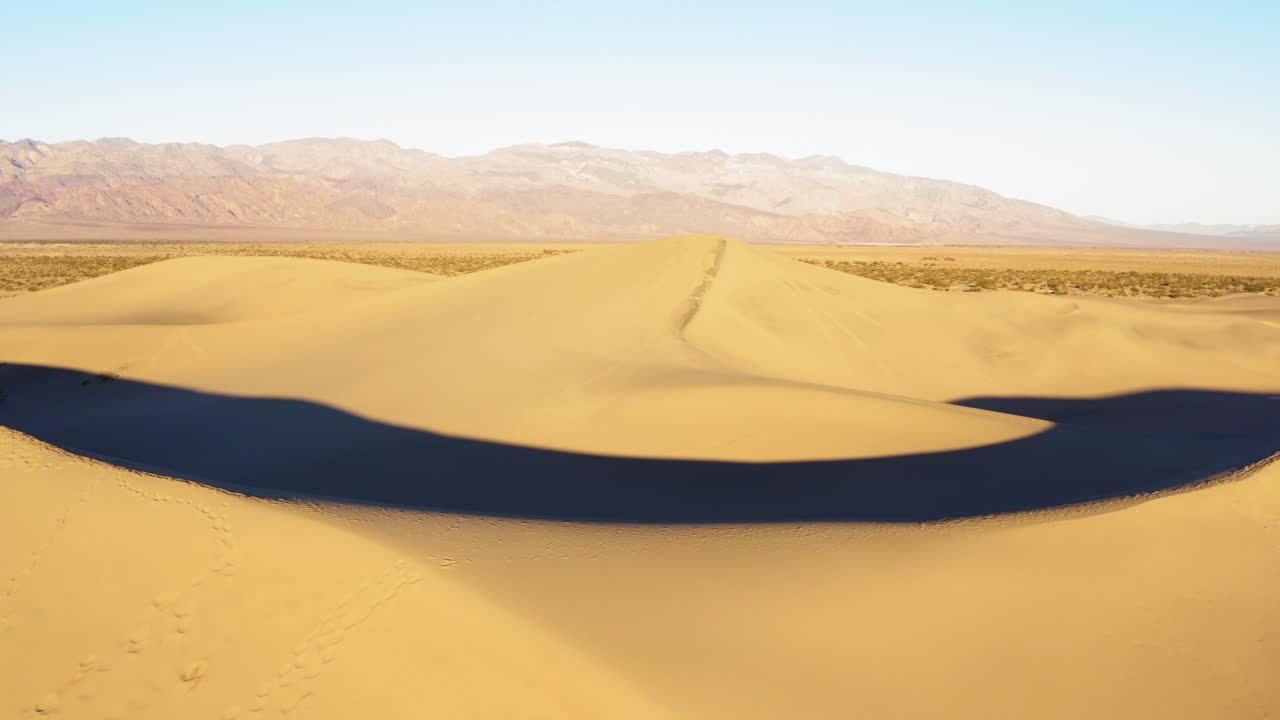 vista de izquierda a derecha de las dunas de arena de mezquite con huellas en ellas en el valle de la muerte, california, ee.uu. con una cordillera al fondo en un día soleado