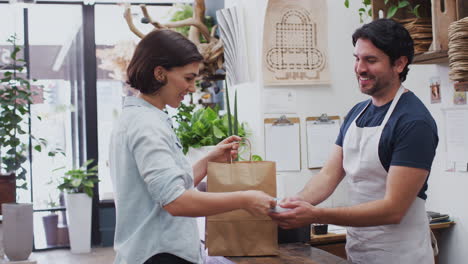 mujer en una floristería haciendo un pago sin contacto en el mostrador de ventas