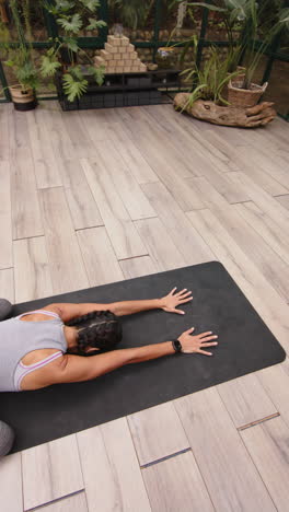 vertical video: practicing yoga, woman stretching on yoga mat in glass house studio
