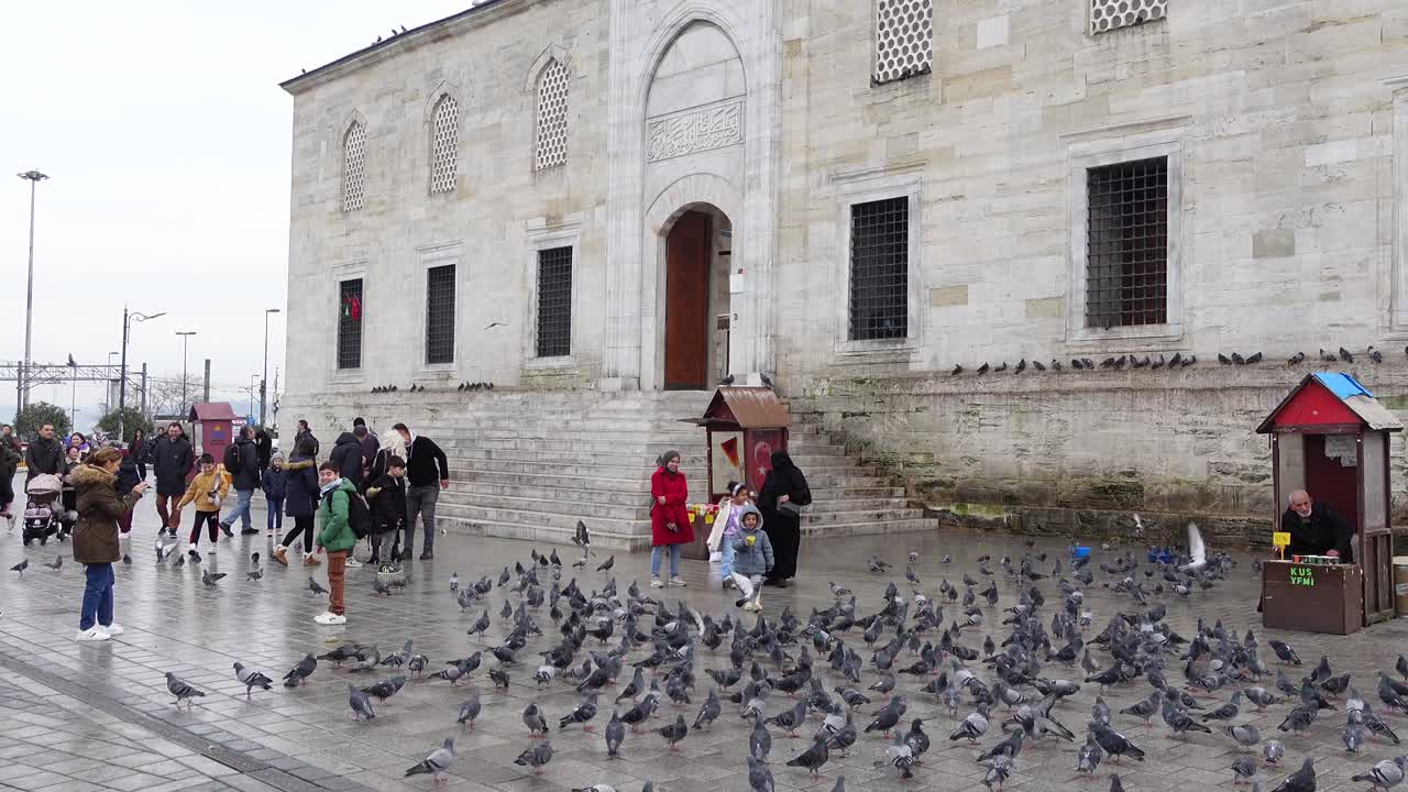 İstanbul'da bir caminin önünde güvercinleri besleyen insanlar.