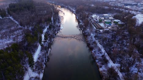 Das-Licht-Der-Morgendämmerung-Spiegelt-Sich-In-Einem-Fluss,-Der-Von-Verschneiten-Wäldern-Umgeben-Ist