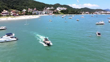 escena aérea de aviones no tripulados de vuelo bajo sobrevolando lanchas rápidas, yates y barcos de lujo con muelle en playa paradisiaca en jurere internacional florianópolis santa catarina