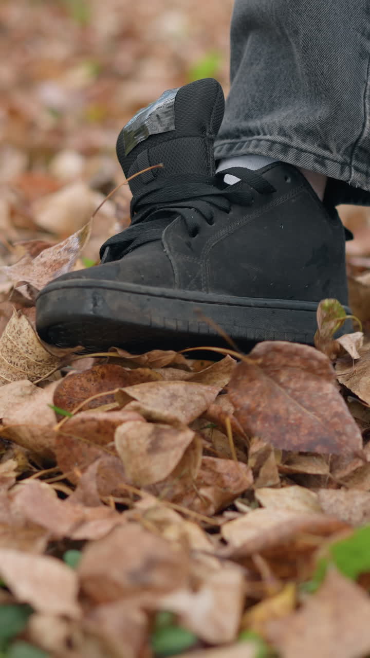 vista de ángulo inferior de alguien caminando y esparciendo follaje seco de otoño con la pierna, mostrando una interacción lúdica con las hojas caídas en el suelo del bosque durante la temporada de otoño