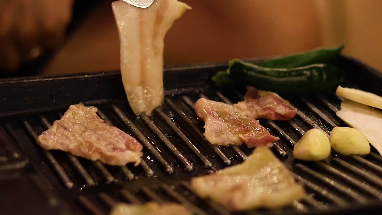 Cooking meat and vegetables on a grill with tongs