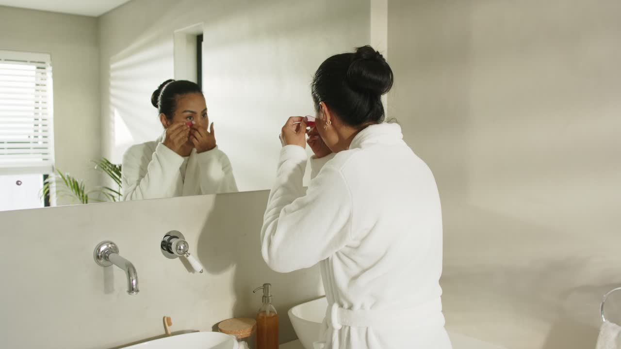 Inspecting reflection, Asian woman opening sachet and applying under-eye patches at vanity mirror