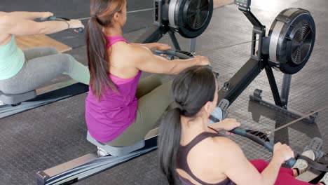 determined unaltered diverse women exercising on rowing machines at gym, in slow motion