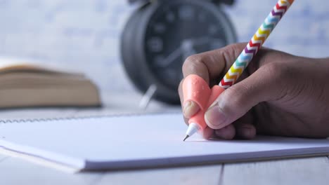 persona que escribe en un cuaderno, con una empuñadura de pluma especial