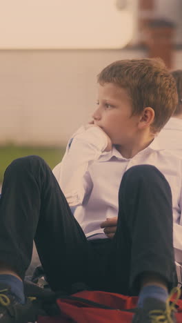 emotional boy throws textbook sitting with school friend and little blond girl with ponytail on pavement after lessons