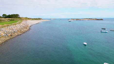 vuelo a lo largo de la costa en bordeos guernsey con mar cristalino y barcos anclados en un día brillante y tranquilo