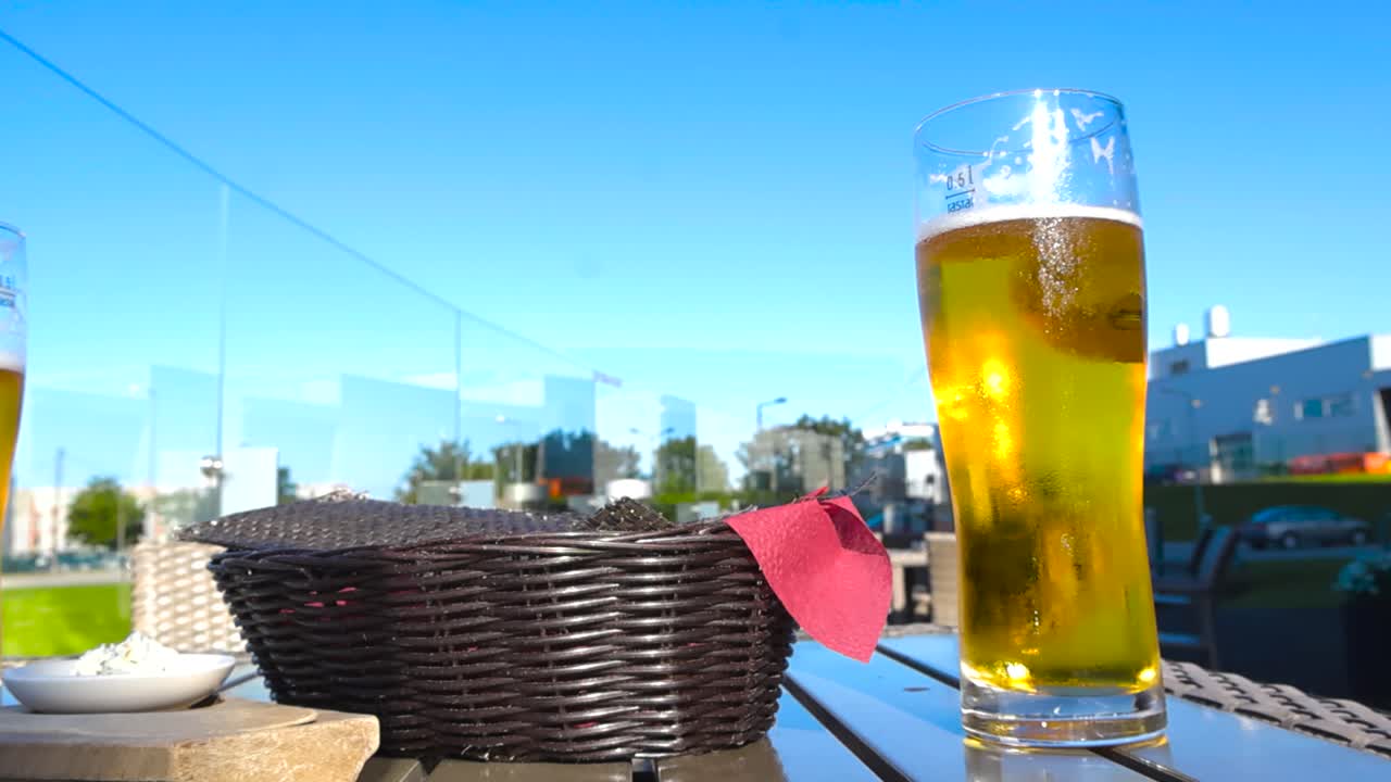 Two golden shiny and foamy beer glasses on an outdoors restaurant table during a sunny summer day with bokeh blurry background blue sky visible in Rocca al mare shoreline