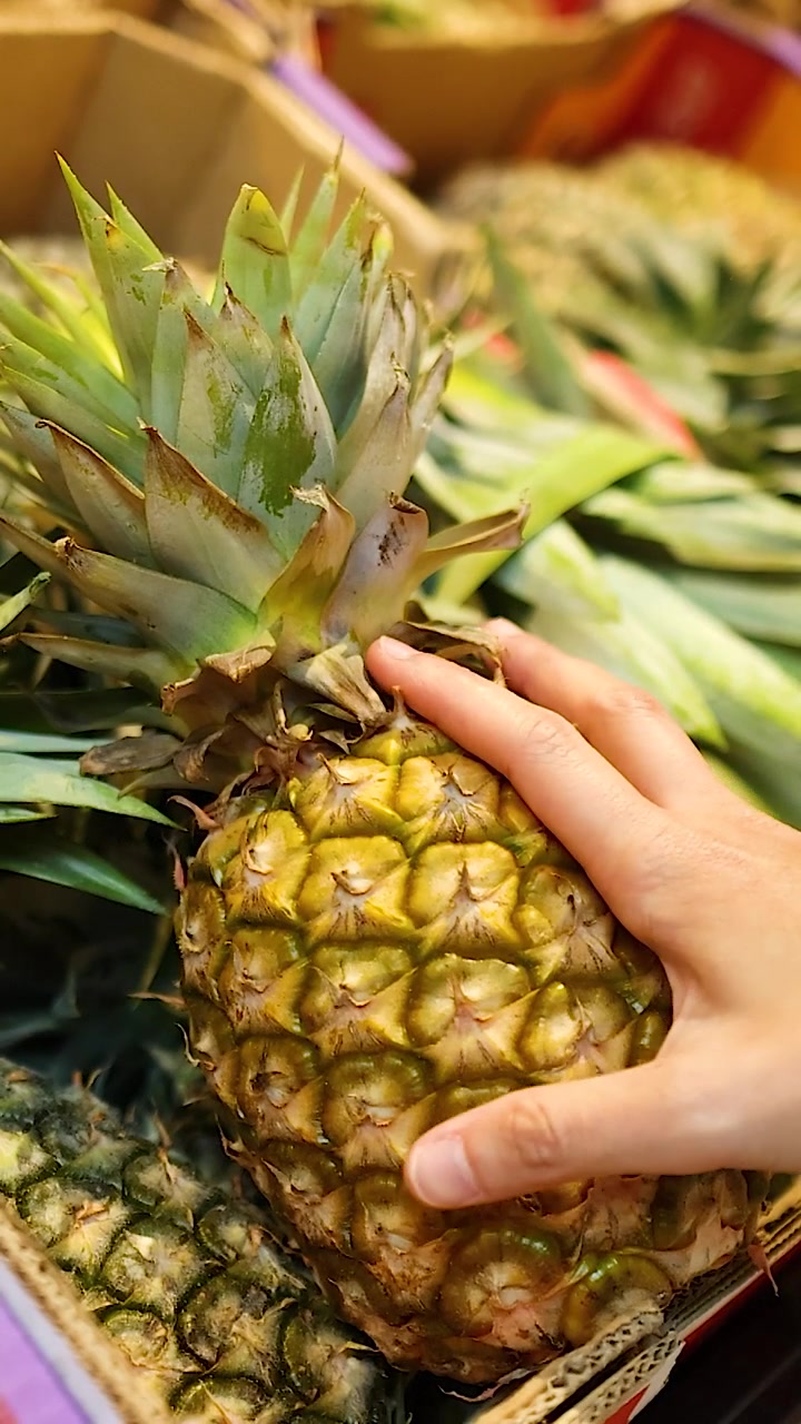 Hands examine a pineapple in a well-lit supermarket setting, highlighting texture and freshness in Gold Coast, Australia