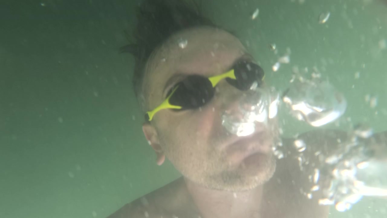 Slow motion underwater close-up portrait of a man wearing swim goggles