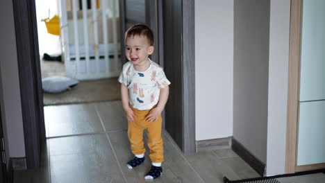 happy toddler boy stands in the room waving hands. kid takes a yellow ball and squeezes it excitedly. top view.
