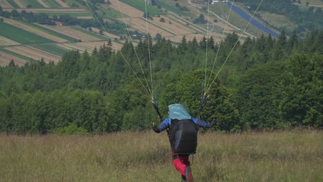 A paraglider sprints forward, his parachute catching the wind, lifting him off the ground into an epic flight over the forest