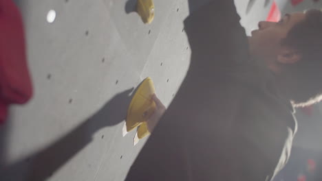 primer plano vertical de un joven atleta masculino escalando una pared de roca artificial en el gimnasio de boulder