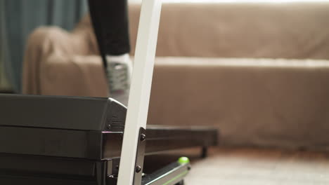 muscular woman races on treadmill at home in hall closeup. sporty woman with lean legs exercises on automatic apparatus in personal gymnasium