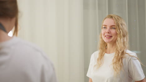 back view of beautician approaching warmly lit salon space as smiling client begins conversation, creating relaxed and friendly atmosphere with mirror lights softly illuminating room interior