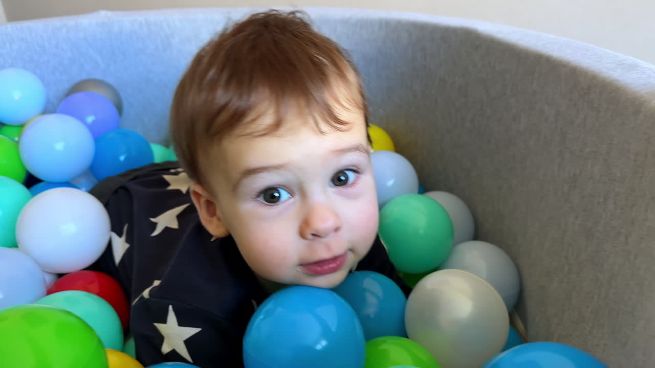 Beautiful Caucasian baby boy in the dry pool indoors. Curious playful child tries hard to reach the camera. Close up.