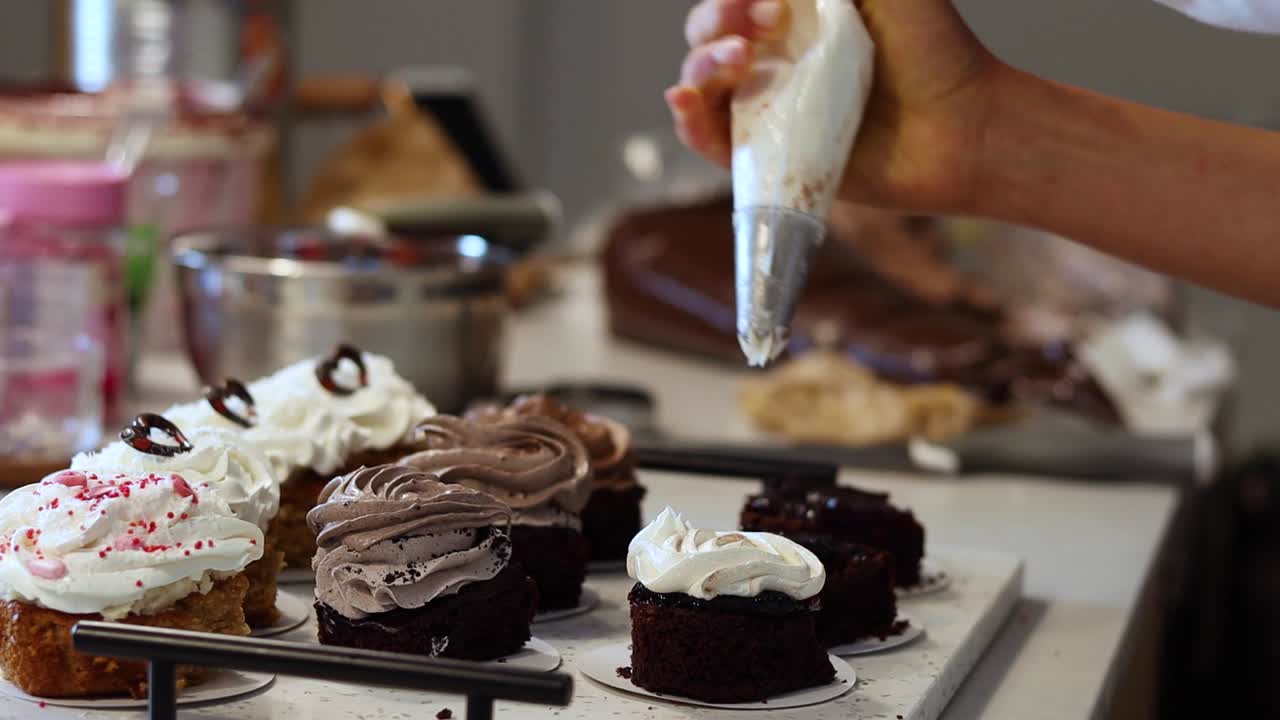 Cocinero de cultivos añadiendo crema batida a los pasteles de esponja en la panadería