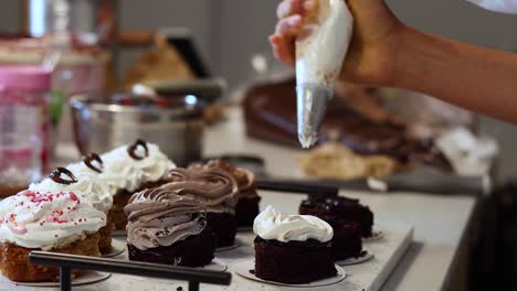 crop cook adding whipped cream on sponge cakes in bakery