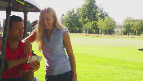 couple playing round on golf together sitting in buggy with score card