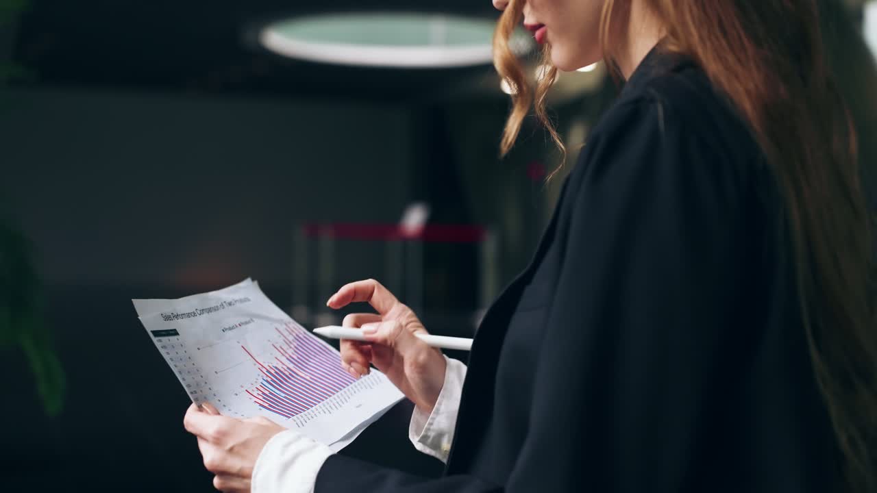 A slow motion close-up of a businesswoman's hands as she carefully reviews financial documents, pointing to data on bar graphs and pie charts in a corporate office