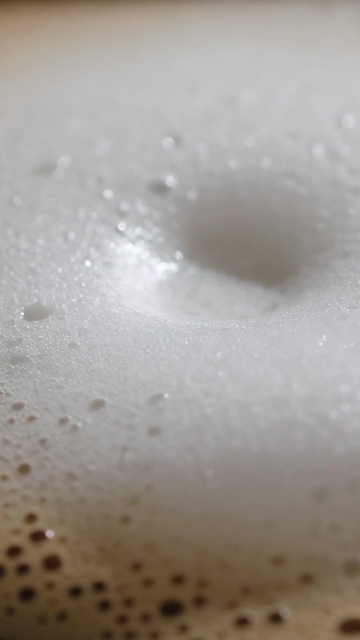 Video verticale: Telecamera in movimento che mostra una fossetta di schiuma che si approfondisce su una tazza sul bancone per la texture, cucchiaino