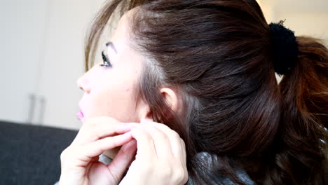 close up of a woman putting on her heart-shaped earring while sitting