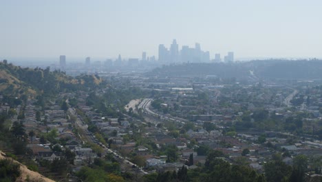 panoramic view of los angeles, with a residential neighborhood in the foreground. the downtown skyline is visible in the distance, with roads and freeways connecting the city